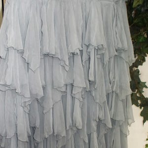 May include: A denim skirt with a light wash, paired with a layered, flowing, gray chiffon skirt. The skirt has a zipper and button closure. The chiffon skirt has multiple layers of ruffles.