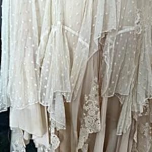 May include: A layered, off-white skirt with multiple textures. The skirt features sheer, dotted fabric, ruffled edges, and delicate lace details. The design creates a flowing, romantic aesthetic, suitable for special occasions.