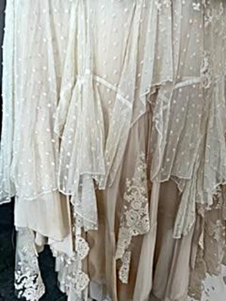 May include: A layered, off-white skirt with multiple textures. The skirt features sheer, dotted fabric, ruffled edges, and delicate lace details. The design creates a flowing, romantic aesthetic, suitable for special occasions.