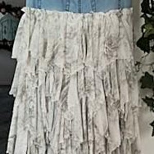May include: A denim skirt with a light blue wash, featuring the waistband and pockets of jeans. The skirt's lower half is a layered, ruffled design in a light gray and white floral pattern, creating a bohemian aesthetic.
