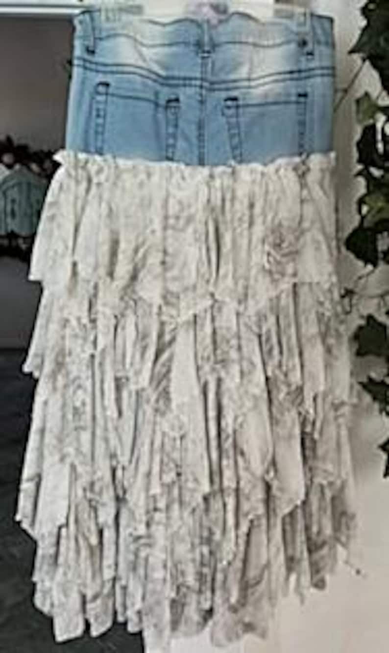 May include: A denim skirt with a light blue wash, featuring the waistband and pockets of jeans. The skirt's lower half is a layered, ruffled design in a light gray and white floral pattern, creating a bohemian aesthetic.