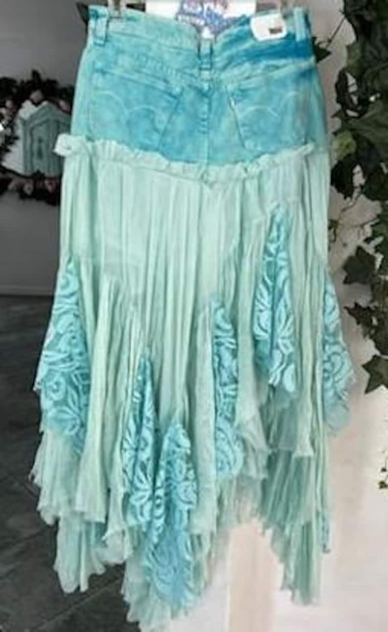 Puede incluir: Falda de mezclilla y encaje en tonos azules y turquesas. La falda presenta una cintura de mezclilla y un dise&ntilde;o fluido y en capas con detalles de encaje. La falda est&aacute; colgada en una percha.