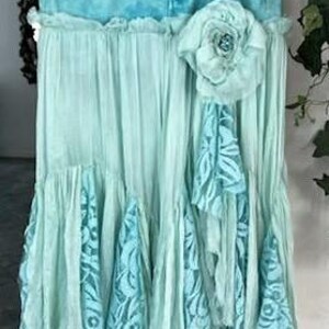 Puede incluir: Falda vaquera turquesa con un dise&ntilde;o en capas y fluido. La falda presenta una cintura vaquera, una gran flor de tela y volantes en cascada con detalles de encaje. La falda mide aproximadamente 76 cm de largo.