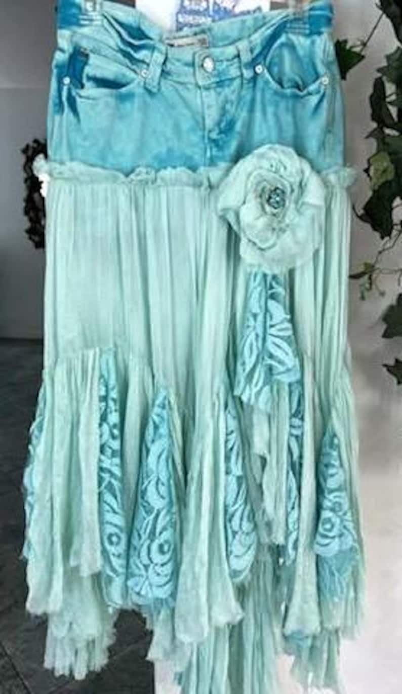 Puede incluir: Falda vaquera turquesa con un dise&ntilde;o en capas y fluido. La falda presenta una cintura vaquera, una gran flor de tela y volantes en cascada con detalles de encaje. La falda mide aproximadamente 76 cm de largo.
