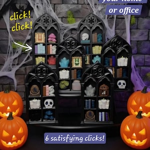May include: A collection of five black gothic-style miniature bookshelves with pointed arches, each containing small decorative items like books, skulls, candles, and framed pictures. The shelves are arranged in a tiered display on a dark surface.