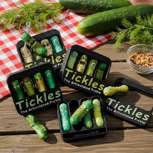 May include: Several black rectangular containers labeled Tickles The Articulated Pickle, each holding small green articulated pickle figures with printed eyes. Some pickles are inside the slots, while others rest outside on the wooden surface.