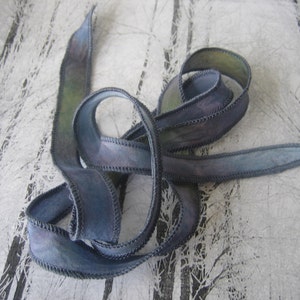 May include: A length of blue ribbon with a stitched edge, featuring a watercolor effect with shades of blue and green. The ribbon is curled and looped, suggesting it's ready for use in crafts or gift wrapping.