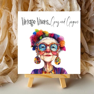 May include: A watercolor illustration of a stylish older woman with large glasses and colorful accessories. The image is on a small wooden easel, with the text "Vintage Vixens... Gray and Gorgeous" at the top.