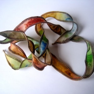 May include: A colorful, abstract ribbon sculpture. The ribbon is a mix of colors including red, orange, yellow, green, and blue. The edges are outlined with a brown stitch. The ribbon is twisted and curled, creating a dynamic and eye-catching design.