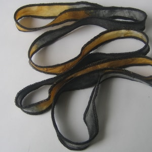 May include: A length of ribbon with a unique design. The ribbon features a black exterior with a yellow-gold interior. The edges are finished with a decorative black stitching. The ribbon is looped and appears to be made of a soft, flexible material.