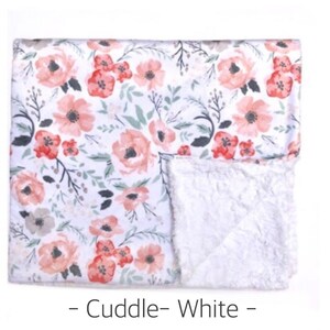 May include: A white and pink floral print baby blanket with a soft white sherpa lining. The blanket has a "Cuddle - White" label.