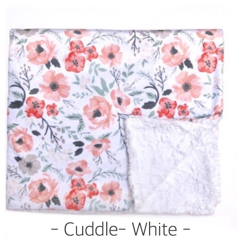 May include: A white and pink floral print baby blanket with a soft white sherpa lining. The blanket has a "Cuddle - White" label.