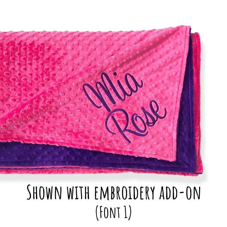 May include: A bright pink dimpled minky blanket with a deep purple underside. The pink side features the name Mia Rose embroidered in a dark purple cursive script. The text below the blanket reads SHOWN WITH EMBROIDERY ADD-ON (FONT 1).