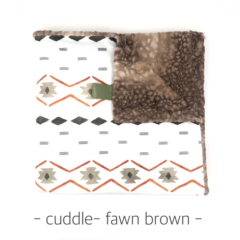 May include: A white and orange geometric patterned baby blanket with a fawn brown faux fur backing. The blanket has a green tag that says "cuddle".