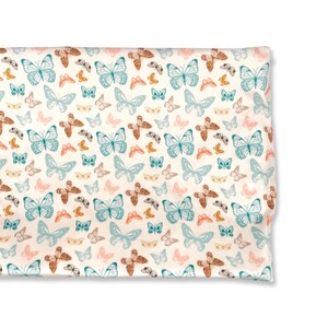 May include: A white fabric with a repeating pattern of blue, brown, and pink butterflies. The butterflies are arranged in a staggered pattern.