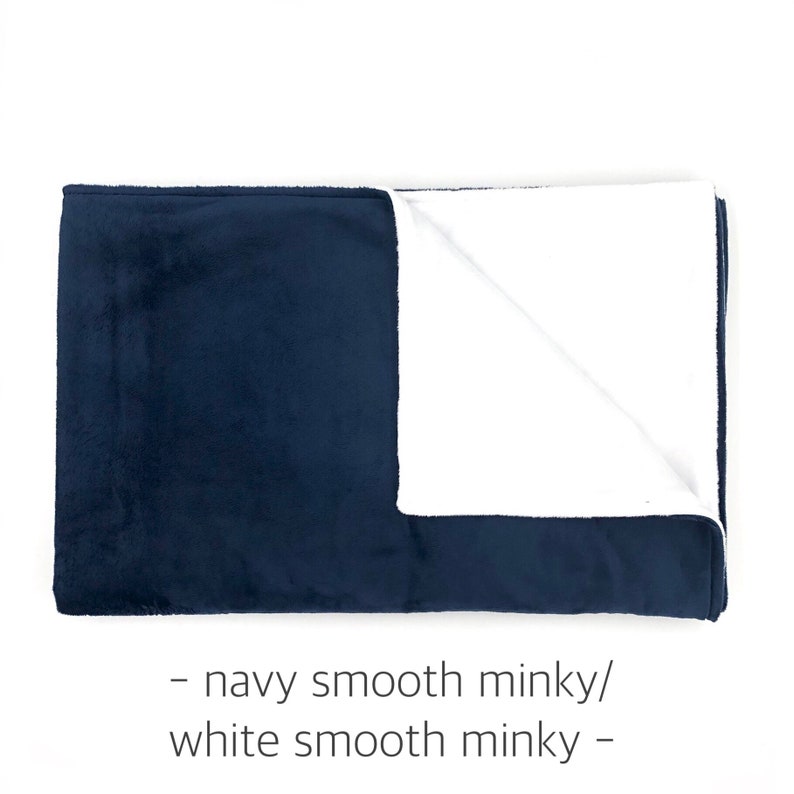 May include: A rectangular blanket featuring a navy blue smooth minky fabric on one side and a white smooth minky fabric on the other, with the text - navy smooth minky/ white smooth minky - printed below the folded fabric.