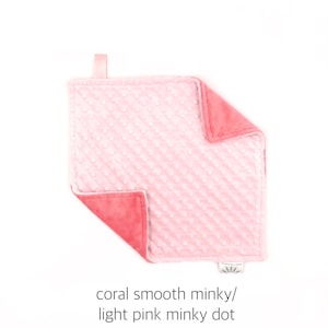 May include: A soft, pink and coral minky baby blanket with a textured dot pattern on one side.  The blanket is made of two different fabrics, one smooth and one with a dot pattern.  The blanket has a loop for hanging.