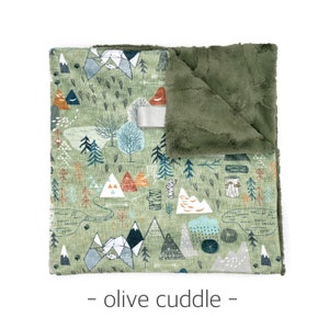 May include: A soft, olive green baby blanket with a mountain and forest pattern. The blanket features a detailed design of trees, mountains, and trails in shades of blue, orange, and green. The reverse side is a plush, olive green fabric.