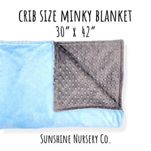 May include: A crib size minky blanket measuring 30 inches by 42 inches. The blanket features a smooth light blue side and a textured gray side with a raised dot pattern. The text reads CRIB SIZE MINKY BLANKET 30 x 42 and Sunshine Nursery Co.