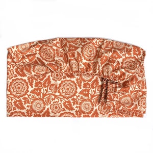 May include: A rust-colored fitted sheet with a white floral pattern. The sheet has a gathered elastic edge.