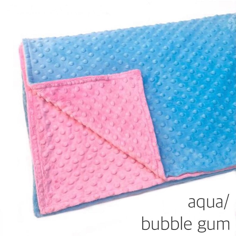 May include: A soft, textured blanket featuring a dimpled minky surface. One side is a bright aqua blue, while the folded corner reveals a contrasting bubble gum pink underside. The text aqua/bubble gum is printed in the bottom right corner.