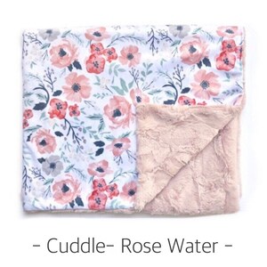 May include: A soft, pink and white floral print baby blanket with a plush, pink minky backing. The blanket is folded in half, showing both sides.