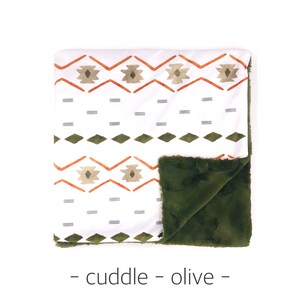 May include: A white and green patterned baby blanket with a soft olive green fleece backing.  The blanket features a geometric pattern with orange, white, and green colors.  The text "cuddle - olive -" is printed below the blanket.