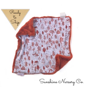 May include: A soft, plush baby blanket with a rust-colored faux fur backing and a white cotton front featuring a repeating pattern of red trees and houses. The blanket is folded in half and the text "Ready to Ship" is visible in the top left corner.