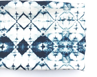 May include: A white fabric with a blue and white tie-dye pattern. The pattern is a repeating diamond shape with a starburst in the center of each diamond.