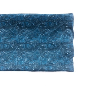 May include: A rectangular piece of fabric featuring a dark navy blue background with a repeating pattern of white line-drawn swirling waves and small dots. The textile has a smooth texture and is folded to display the continuous graphic design.