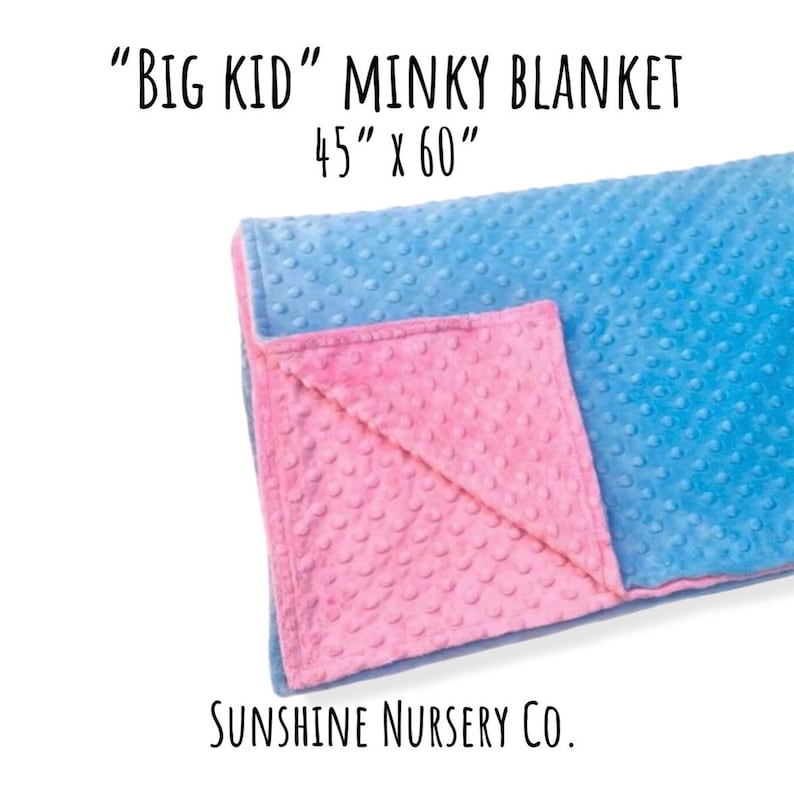 May include: A minky blanket with a textured dot pattern, featuring a bright blue side and a pink side. The text reads "BIG KID" MINKY BLANKET 45" x 60" and SUNSHINE NURSERY CO. The blanket is folded to show both colors.