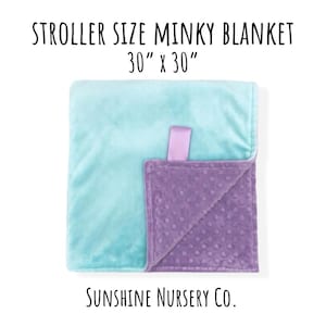May include: A square minky blanket measuring 30 inches by 30 inches, featuring a smooth light blue side and a textured purple side with raised dots. A purple fabric tag is attached to the edge. Text reads: STROLLER SIZE MINKY BLANKET 30" x 30" SUNSHINE NURSERY CO.