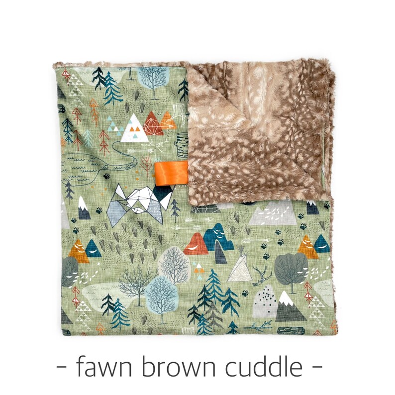 May include: A baby blanket with a forest and mountain design in shades of green, blue, and orange. The blanket has a soft, brown, faux fur backing. An orange ribbon tag is attached to the blanket. The text "- fawn brown cuddle -" is at the bottom.