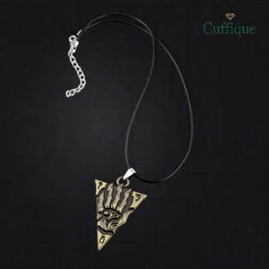 Puede incluir: Un collar con colgante de color bronce con un diseño triangular. El colgante presenta un motivo estilizado de sol u ojo con intrincados detalles recortados. El collar tiene un cordón negro y una cadena plateada.