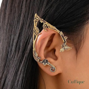 Puede incluir: Un pendiente de oreja dorado con un diseño floral y de hojas. El pendiente se envuelve alrededor de la oreja, con rosas y hojas adornando los bordes. La palabra "Cuffique" es visible en la esquina inferior derecha.