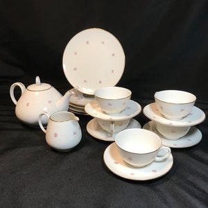 May include: A white tea set with pink floral accents. The set includes a teapot, creamer, sugar bowl, and four teacups and saucers.