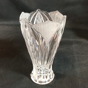 May include: A clear glass vase with a textured, floral design. The vase has a wide mouth and a narrow base.