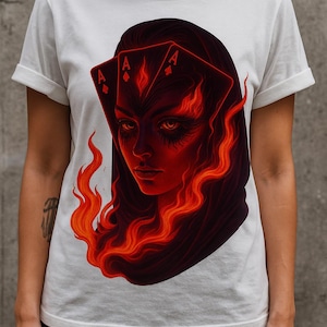 May include: White t-shirt featuring a striking graphic of a woman's face with fiery red hair and playing cards. The artwork depicts the face of a woman with flames and three Ace cards. The design is a bold statement piece.