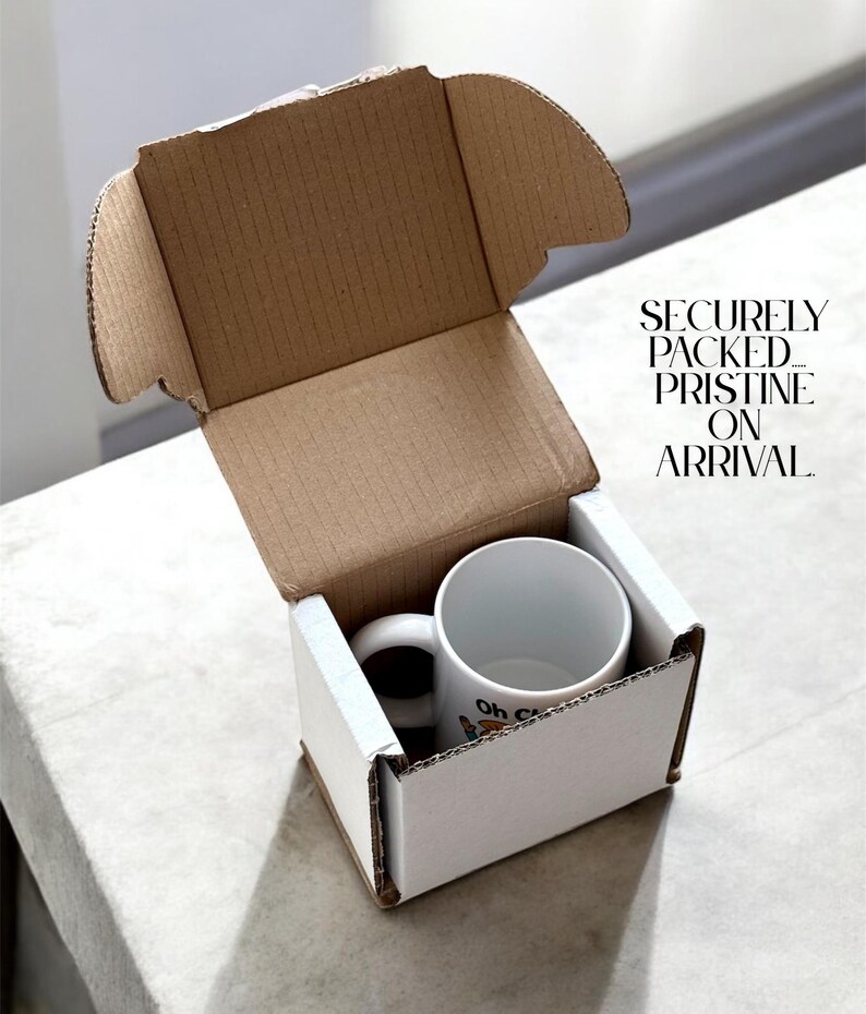May include: A white ceramic mug with a black handle inside a white cardboard box. The mug has a cartoon design and the words "Oh C" printed on it. The box is inside a larger brown cardboard box. Text on the box reads "SECURELY PACKED. PRISTINE ON ARRIVAL."