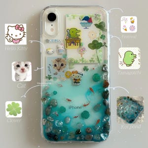Puede incluir: Funda transparente para iPhone con un diseño decorativo que presenta a Hello Kitty, un gato y un estanque de carpas koi. La funda incluye un trébol, un personaje de Tamagotchi y la palabra "Festival". La funda tiene un diseño azul y verde similar al agua con pequeñas piedras y peces.