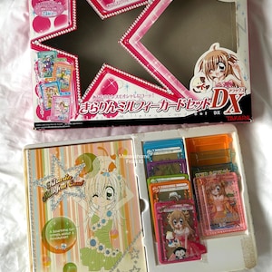 May include: A Kirarin Revolution Millefeui Card Set DX featuring a pink star-shaped cardboard box with anime character illustrations and Japanese text, alongside a plastic tray containing a card binder and multiple colorful transparent character cards.
