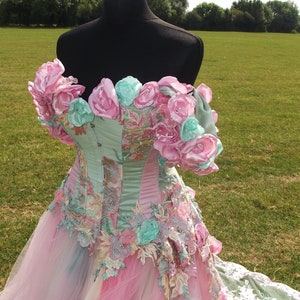 Puede incluir: Un vestido de novia rosa y verde con un corpi&ntilde;o de cors&eacute; y una falda de tul. El corpi&ntilde;o est&aacute; adornado con flores de tela rosa y verde. La falda est&aacute; hecha de capas de tul y tiene un borde de encaje.