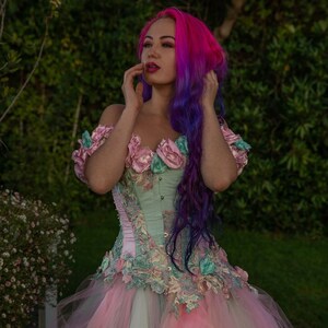 Puede incluir: Una mujer con cabello rosa y morado lleva un cors&eacute; verde claro y rosa con adornos florales y una falda de tul a juego.