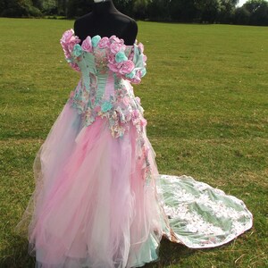 Puede incluir: Un vestido de novia de tul rosa y verde con adornos florales y una larga cola.