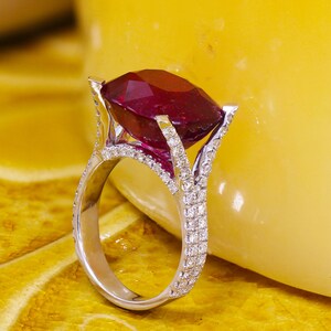 May include: A silver ring with a large, deep red gemstone surrounded by smaller white gemstones.