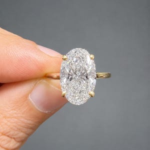 Op de afbeelding: Een gouden ring met een grote, ovaal geslepen diamant. De diamant is helder en sprankelend. De band van de ring is van effen goud. De zetting heeft vier klauwen die de diamant vasthouden.