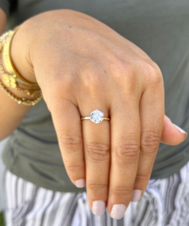 Op de afbeelding: Een close-up van een hand met een gouden ring met een grote, ronde, heldere diamant.