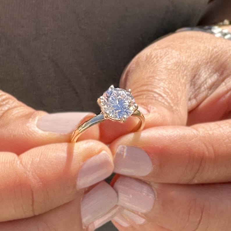 Op de afbeelding: Een gouden verlovingsring met een grote, heldere, ronde diamant.
