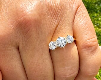 Può includere: Un anello di fidanzamento in oro con tre diamanti, una pietra centrale grande e due pietre più piccole su entrambi i lati.