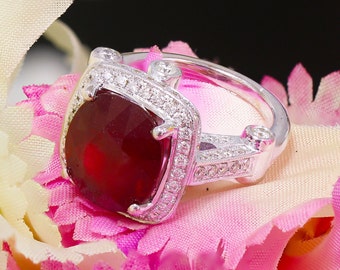 May include: A silver ring with a large, red gemstone surrounded by smaller, clear gemstones.